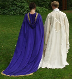 A couple dressed in custom made wedding garb consisting of a long purple cloak with gold trim and train and a white replica Saruman wizard's robe.